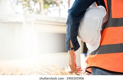 Back View Of Environmental Engineering Standing And Holding Hardhat At The Work Site. Background Of Modern Office Buildings With Park