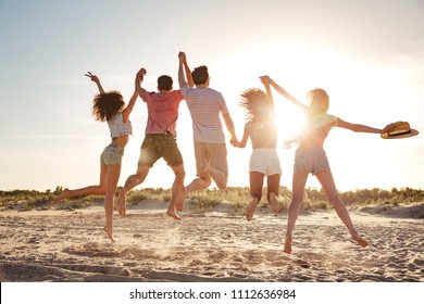 Vista posterior de jóvenes amigos emocionados vestidos con ropa de verano saltando juntos con las manos levantadas en la playa