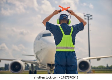 Back view of an experienced ground marshaller making the stop signal to the cockpit crew