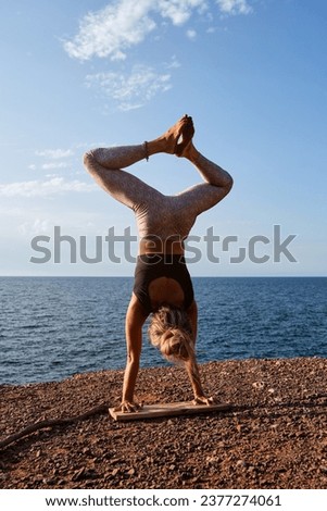 Back view of faceless female athlete in sportswear standing on wooden plank in adho mukha vrikshasana pose with legs in baddha konasana while practicing yoga on beach