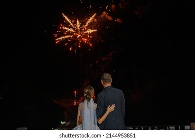 Back view of faceless married couple, hugging each other and watching to amazing flares and fireworks explode in  night sky with colorful pyrotechnic display during wedding day