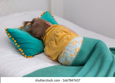 Back View Of Fair Toddler Girl In Yellow Top Lying Down In Bed Relaxing Under Turquoise Throw Blanket