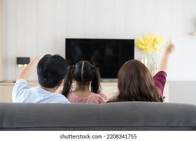 Back view of family with child daughter embracing together and watching tv while sitting on sofa in living room at home. Happy father, mother and daughter spending time together at home - Powered by Shutterstock