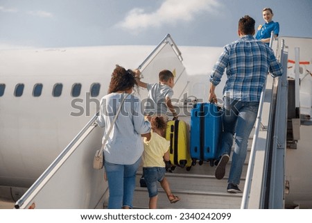 Back view of family of four getting on, boarding the plane on a daytime, ready for summer vacations. People, traveling, vacation concept