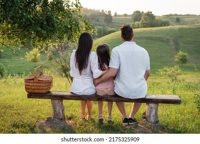 back view of family sitting on bench near wicker basket in front on scenic landscape