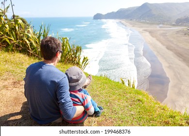 back view of family sitting at the top of lion rock at piha beach, new zealand