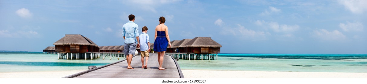 Back View Of A Family Walking On Wooden Jetty During Summer Vacation At Luxury Resort