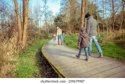 Back view of family walking together holding hands over a wooden pathway into the forest