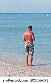 Back View, Far Distance Of A Hispanic Male, Standing In Tropical, Shoreline, Water, Reading A Text Message