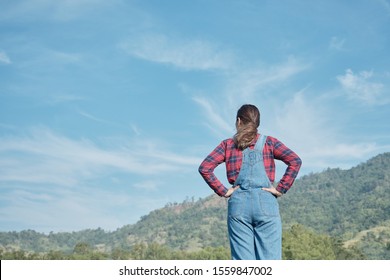 Back view of farmer woman in plaid shirt and blue jean pose  hand on her waist stand on her land looking at blue sky