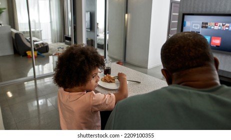 Back View Of Father And Curly Little Son Having Lunch Or Dinner With Pizza At Table At Home Kitchen. Unhealthy Eating. Young Black Family Lifestyle And Relationship. Fatherhood And Parenting