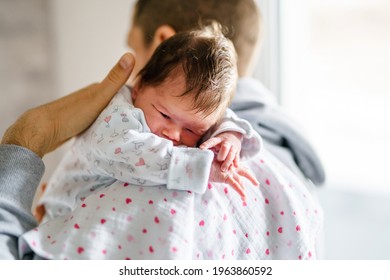 Back view of father holding his newborn baby over the shoulder while standing by the window in day at home - sleepy infant in position for burping new life and parenthood father's day concept