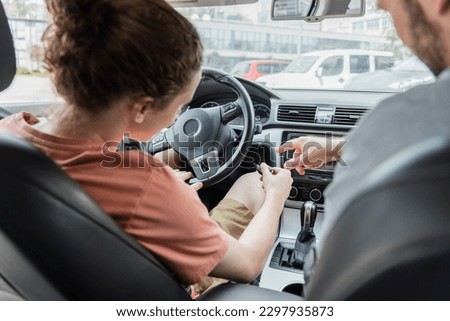 back view of father pointing with finger while showing teenage son how to start car