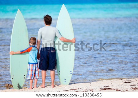 Back view of father and son with surfboards at beach