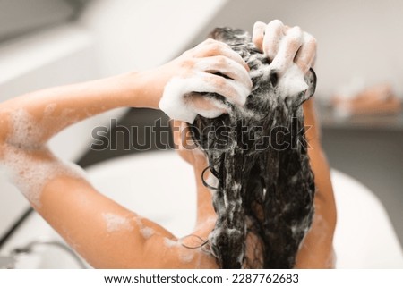 Back View Of Female Applying Shampoo And Washing Head Taking Bath In Modern Bathroom Indoor. Woman Doing Haircare Routine Using Cosmetics. Beauty And Hair Care Concept. Selective Focus