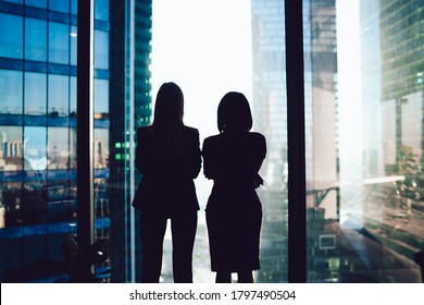 Back View Of Female Colleagues In Formal Wear Standing Near Window Looking At Modern Exterior Of Skyscrapers In Business Center, Silhouette Of Women Together Planning Future Success Of Brainstorming