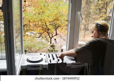 BAck view of female Dj playing music on modern midi controller turntable while standing near the open window. Digital device for mixing music on events and in studio