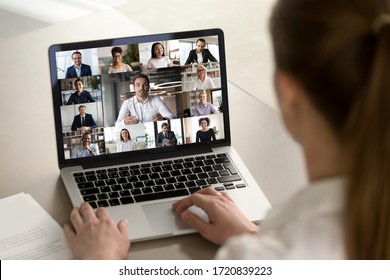 Back view of female employee engaged in web team meeting briefing using laptop at home, have webcam conference, woman worker talk on video call with diverse multiracial colleagues on computer