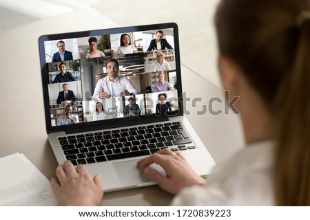Back view of female employee engaged in web team meeting briefing using laptop at home, have webcam conference, woman worker talk on video call with diverse multiracial colleagues on computer