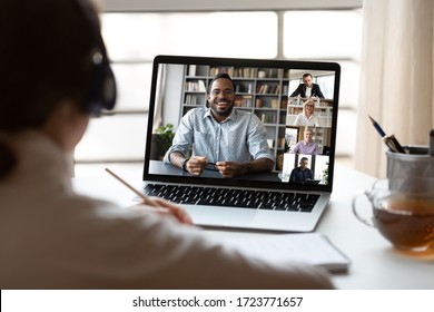 Back view of female employee have webcam conference on computer with multiracial colleagues, woman talk brainstorm on video call with diverse coworkers, engaged in web team online briefing from home