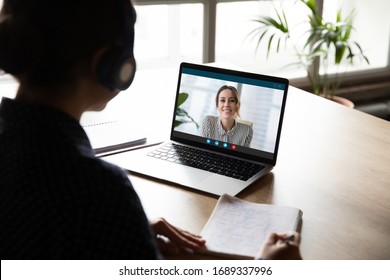 Back view of female employee sit at desk at home have Webcam conference on laptop with business partner or client, woman worker talk on video call with coworker or consultant, watch online webinar