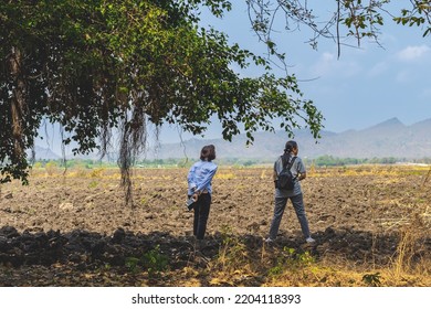 Back View Of Female Farmer Friend Holding Mobile Phone And Discuss Soil Quality For Farming In Field. Agriculturist Women Consult Each Other About Cultivation In Meadow. Farm And Agricultural Business