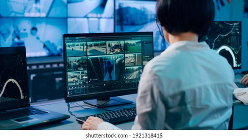 Back view of female operator watching surveillance camera footages and identifying man while working in contemporary security center with male colleague - Shutterstock ID 1921318415