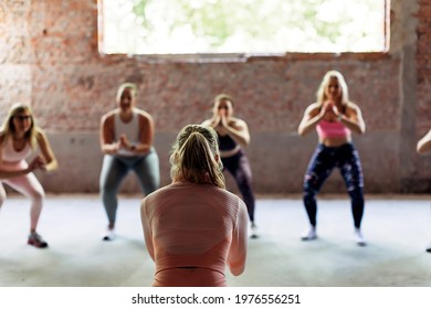 Back View Of Female Personal Trainer Giving Fitness Class To A Group Of Sporty Women Indoors. Sports And Healthy Lifestyle.