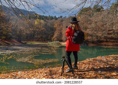 Back view of female photographer in red jacket and black hat taking photos in sevenlakes (yedigoller), Bolu, Turkey 