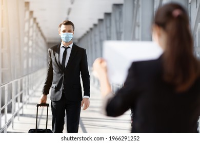 Back View Of Female Representative Meeting Business Partner In Airport, Holding Placard With His Name. Businessman In Face Mask Arrived For Business Meeting, Reading Names On Boards