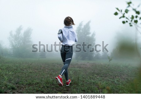 Back view of female runner jogging in nature on foggy morning. Copy space.