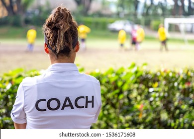 Back view of a female soccer, football, coach in white coach shirt watching her team play at an outdoor football field - Powered by Shutterstock