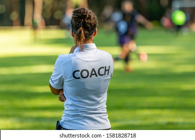 Back view of a female sport coach watching her team compete at an outdoor football field