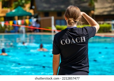 Back view of female swimming coach, wearing COACH shirt, working at an outdoor swimming pool and watching her swimmers competing - Shutterstock ID 2212857477