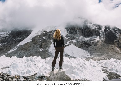 Back View Of Female Tourist With Blonde Curly Hair Standing Outdoors And Enjoying Foggy Himalayas During Exiting Travel Lifestyle.Woman Hiker Wanderlust Traveling In Mountains With Panorama Of Slopes