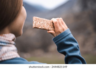 Back view of female traveler eating a grain cereal bar snack on the hike, woman takes a break with dessert, concept muesli, healthy food, hiking, tourism, sports, active, outdoor lifestyle - Powered by Shutterstock