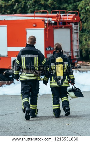 back view of firefighters in fireproof uniform walking on street with fire truck behind