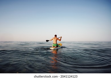 Back View Of Fit Man Floating On Paddle Board In The Sea