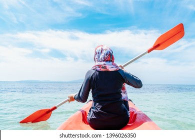 Back View Of A Fit Young Muslim Woman Kayaking On The Beach. Woman Paddling A Kayak By The Tropical Beach. Kayaking Tour In Phuket, Thailand. Travel Concept.