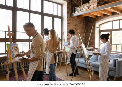 Back view five young multiethnic painters engaged in group art-class, painting on canvas looking focused, attend lesson creative hobby in modern spacious loft room. Education, develop skills concept