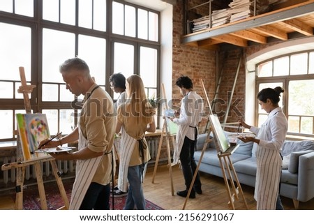 Back view five young multiethnic painters engaged in group art-class, painting on canvas looking focused, attend lesson creative hobby in modern spacious loft room. Education, develop skills concept