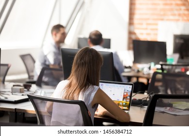 Back View Of Focused Female Millennial Employee Work On Laptop In Shared Office, Concentrated Young Woman Worker Or Intern Use Computer In Coworking Space, Browsing Internet Or Check Mail