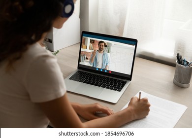 Back View Focused Young Woman In Headphones Looking At Computer Screen, Holding Video Call Online Private Lesson With Male Teacher Native Speaker, Learning Foreign Language Distantly At Home.