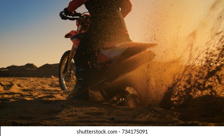 Back View Footage Of The Professional Rider On The FMX Dirt Bike Twisting Full Throttle Handle And Digging Into The Sand With His Back Wheel.