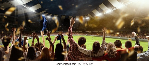 Back view of football, soccer fans cheering their team, holding flag at crowded stadium at evening time. Concept of sport, cup, world, team, event, competition, hobby, lifestyle, emotions - Shutterstock ID 2247122439