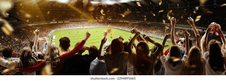 Back view of football, soccer fans cheering their team with flag and posotove emotions at crowded stadium at evening time. Concept of sport, cup, world, team, event, competition