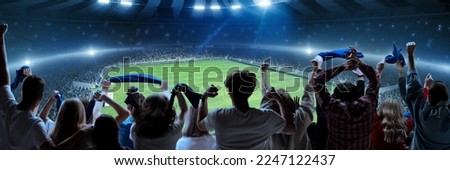 Back view of football, soccer fans cheering their team, holding flag at crowded stadium at evening time. Burst of emotions. Concept of sport, cup, world, team, event, competition, hobby