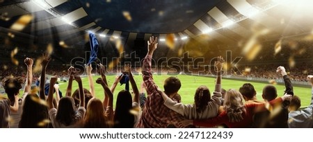 Back view of football, soccer fans cheering their team, holding flag at crowded stadium at evening time. Concept of sport, cup, world, team, event, competition, hobby, lifestyle, emotions