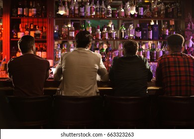 Back view of four young men drinking beer and talking while sitting at bar counter in a modern urban cafe
