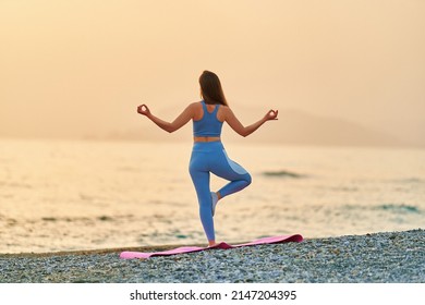 Back View Of Free Calm Serene Bliss Satisfied Fitness Woman Doing Yoga Exercise On The Beach By The Sea. Mental Mind Care And Healthy Habits